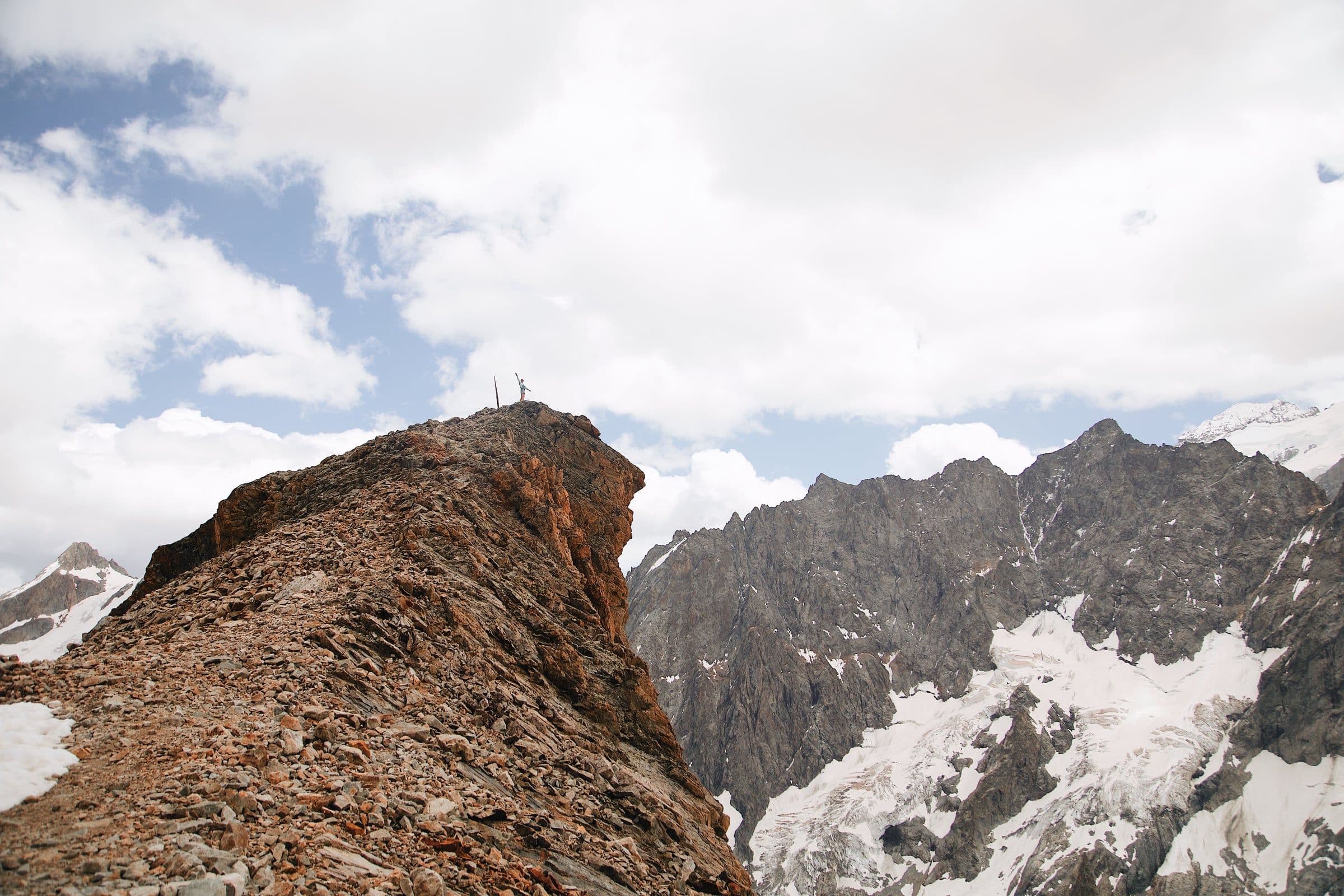 A climber on a wind-scoured rock ridge above a glacier, mid-alpine traverse